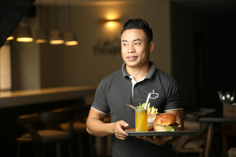 A waiter carrying a tray with a burger, fries and a drink