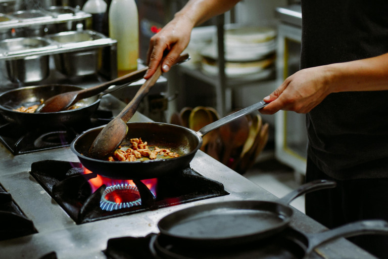 A cook tossing a pan over a gas flame in a busy kitchen